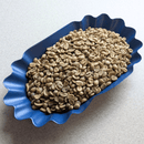 Raw green coffee beans piled in a blue scalloped dish on a light gray surface.